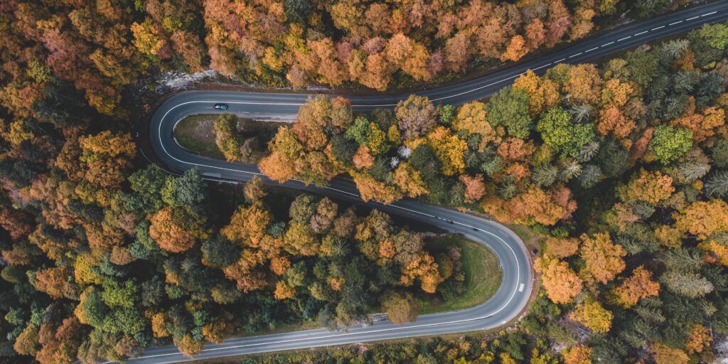 EVORA Global Navigating sustainable Finance. Car driving through winding mountain road surrounded by forest.